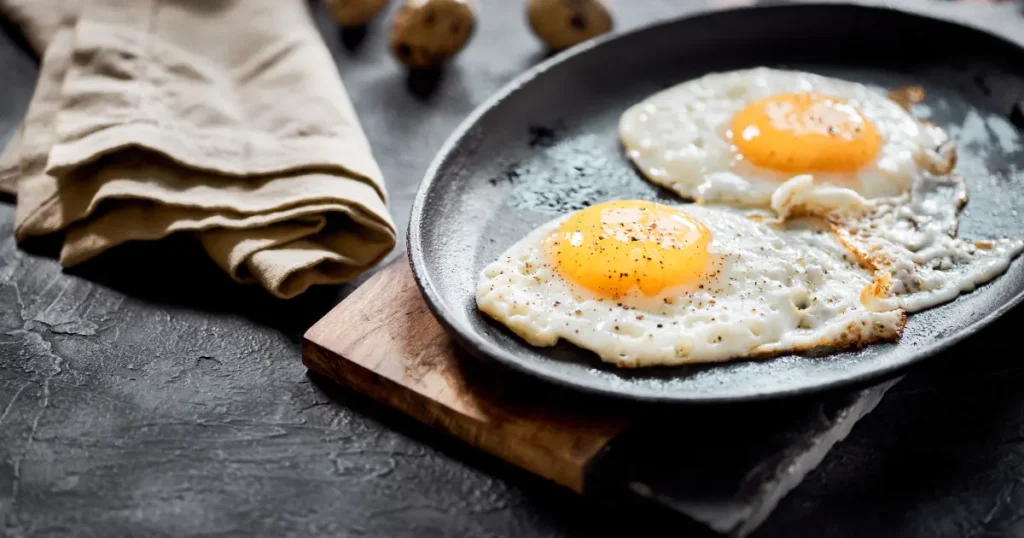 A nutritious breakfast plate featuring two fried eggs, prepared sunny-side up with olive oil, served alongside slices of avocado and a small portion of spinach, specifically tailored for a PCOS-friendly diet.