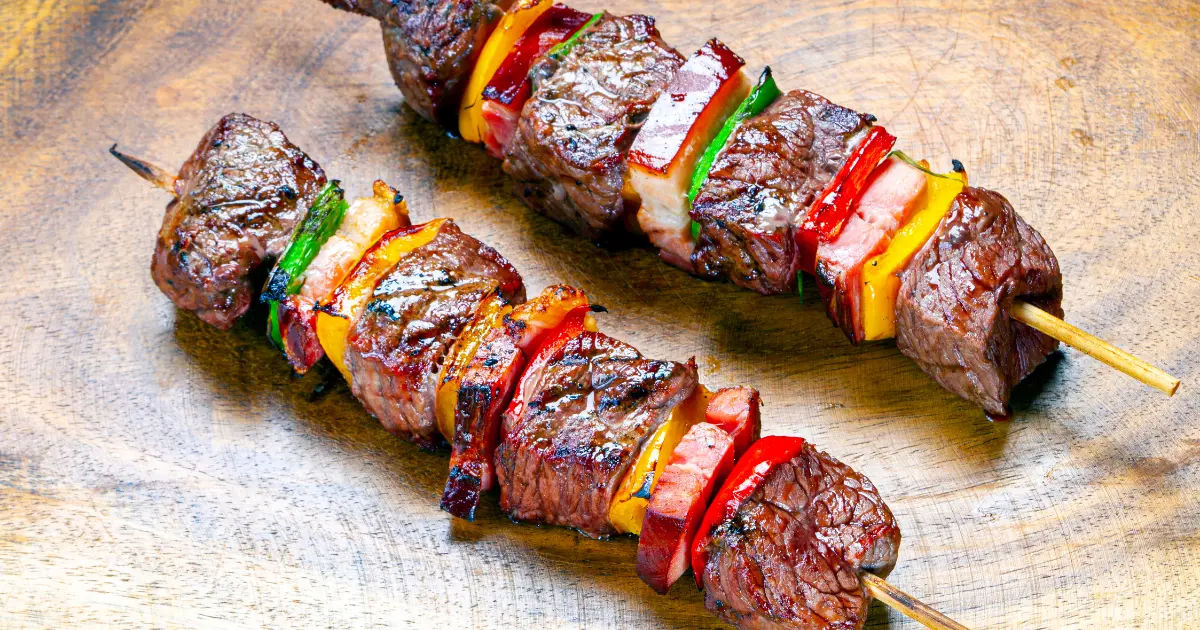 An image of gluten-free grilled meat skewers interspersed with pieces of red and green bell peppers, cooked to a perfect char.