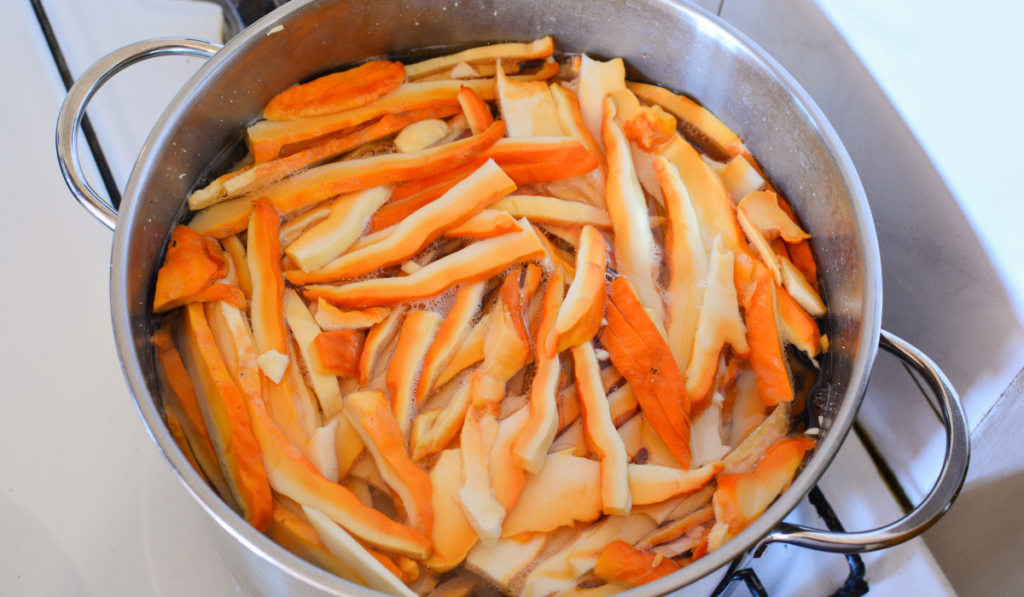 Sliced Chicken of the Woods mushrooms simmering in a stainless steel pot filled with water, exhibiting their vibrant orange and pale undersides."