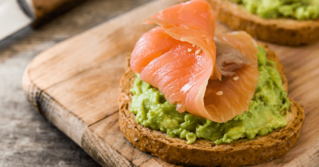 Crispy toast topped with mashed avocado, slices of smoked salmon, and a poached egg, sprinkled with black pepper and herbs, a modern twist on salmon breakfast recipes.