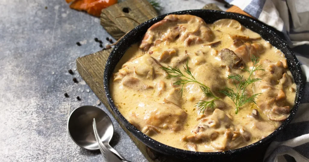 A photo of chicken prepared using the Fricassee method, showing tender pieces of chicken in a creamy, white sauce with herbs, served in a deep, elegant dish.