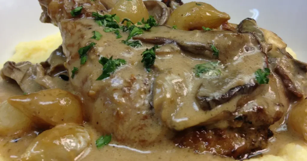 A photo of a plate of chicken fricassee, featuring tender chicken pieces simmered in a creamy, light sauce with mushrooms and herbs, served alongside steamed rice and fresh parsley garnish.