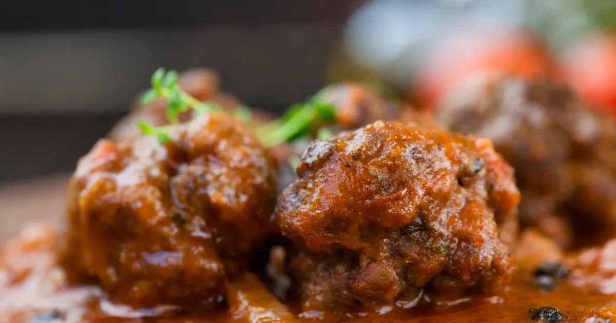 A photo of meat cooked using the Fricassee method, featuring tender, lightly browned pieces simmered in a rich, creamy sauce with visible herbs and vegetables, served in a shallow bowl.