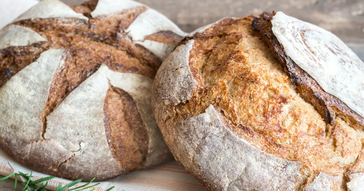 A freshly baked sourdough loaf sliced on a wooden cutting board, accompanied by various breakfast items including butter, jam, and fresh fruits, ready for a wholesome morning meal