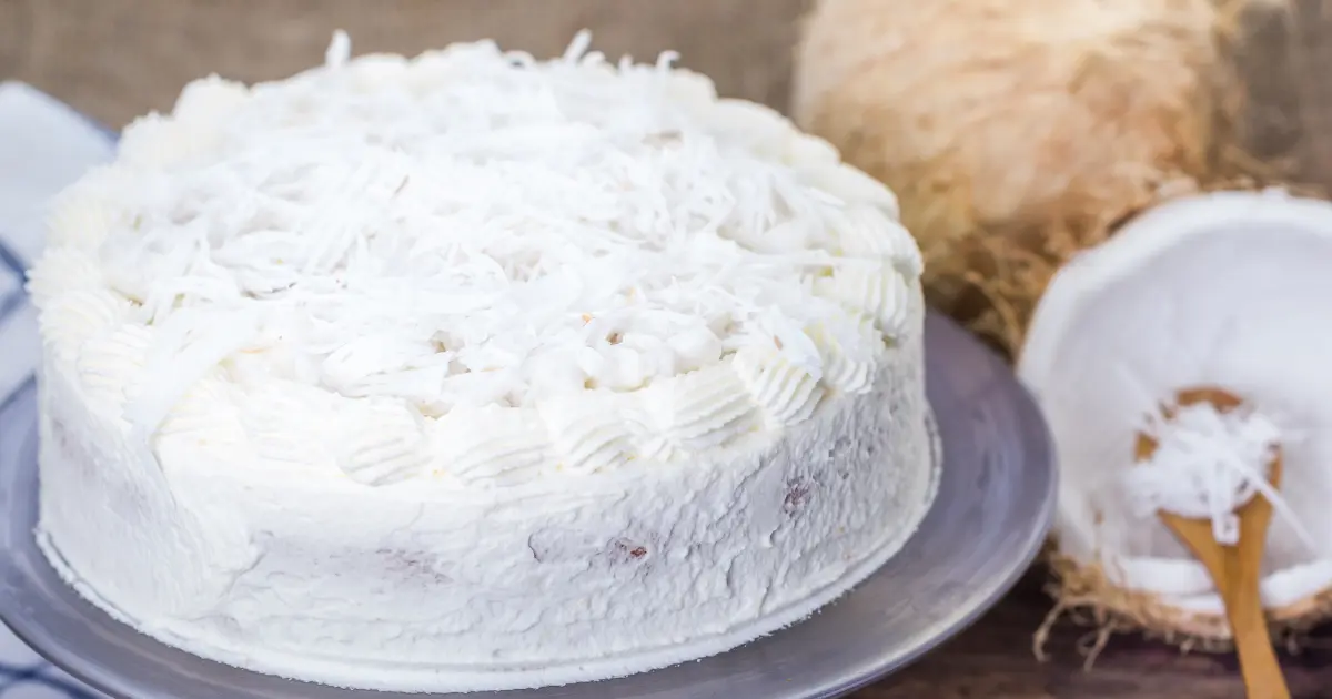 A layered coconut cake with fluffy white frosting and a generous coating of shredded coconut, displayed on a decorative plate, embodying a classic and elegant dessert presentation.