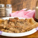 A plate with assorted leftover food next to a nearly full cup of milk.