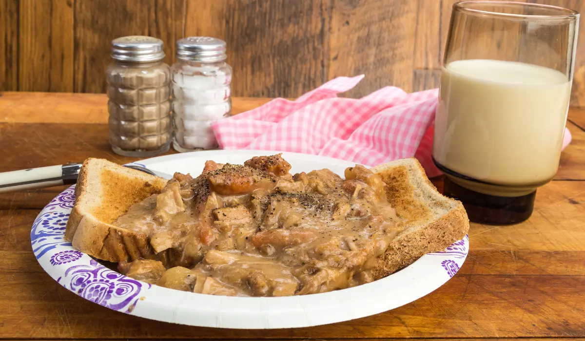 A plate with assorted leftover food next to a nearly full cup of milk.