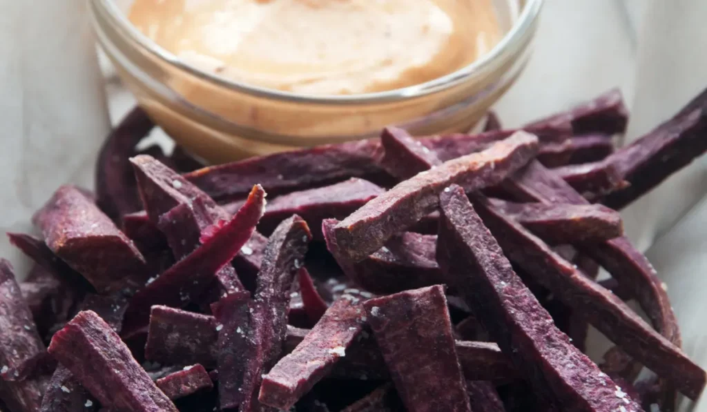 crispy purple sweet potato fries arranged on a plate, accompanied by a dipping sauce.