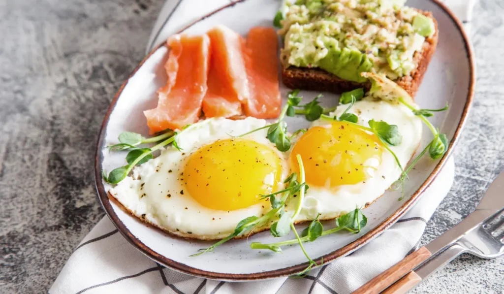 A delicious breakfast plate featuring perfectly cooked salmon fillet and sunny-side-up eggs, garnished with fresh herbs and a slice of lemon.