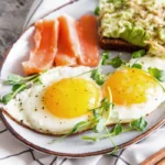 A delicious breakfast plate featuring perfectly cooked salmon fillet and sunny-side-up eggs, garnished with fresh herbs and a slice of lemon.